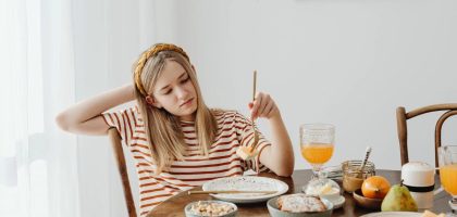Teen girl in striped shirt at breakfast table with fruits, bread, and juice. Casual morning setting.