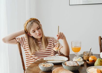 Teen girl in striped shirt at breakfast table with fruits, bread, and juice. Casual morning setting.