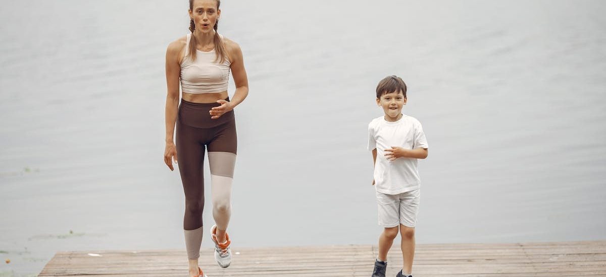 A woman and young boy jogging together on a wooden pier by a tranquil lake, enjoying leisure time outdoors.