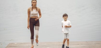 A woman and young boy jogging together on a wooden pier by a tranquil lake, enjoying leisure time outdoors.