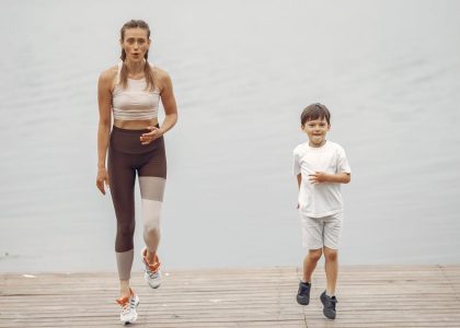 A woman and young boy jogging together on a wooden pier by a tranquil lake, enjoying leisure time outdoors.