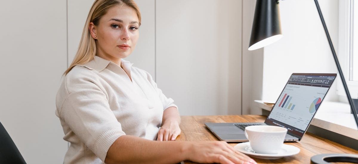 Confident woman working on a laptop in a modern office with data charts displayed.