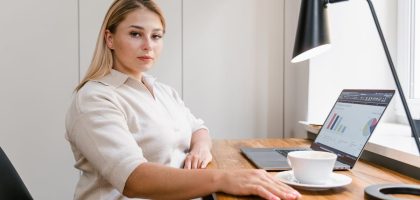 Confident woman working on a laptop in a modern office with data charts displayed.