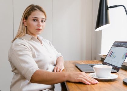 Confident woman working on a laptop in a modern office with data charts displayed.